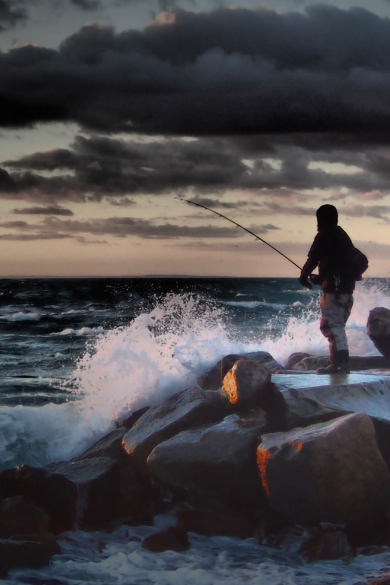 Guy standing on rocks fishing with large waves